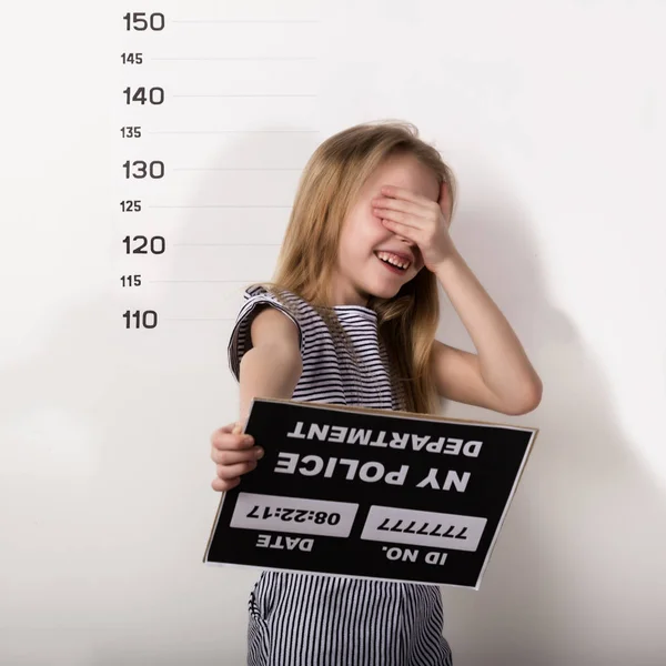 Junge schöne blonde Kind mit einem Schild bedeckt sein Gesicht mit seiner Hand, kriminelle Tasse Schüsse — Stockfoto