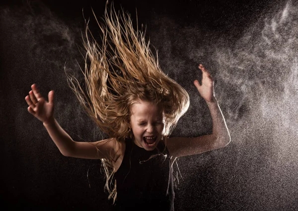 Junges Mädchen mit lebendigen Emotionen, das unter Wassertropfen tanzt. Kind planscht Wasser auf dunklem Hintergrund — Stockfoto