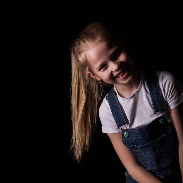 Hermosa niña rubia sobre un fondo oscuro. Ella se para en diferentes poses y muestra diferentes emociones. espacio libre para su texto — Foto de Stock