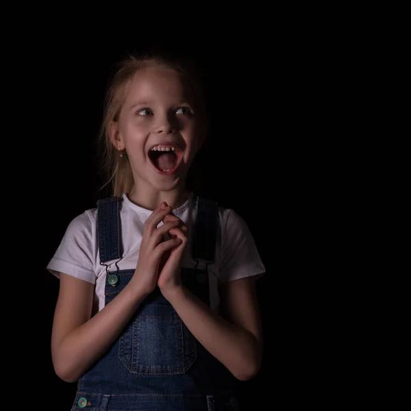 Hermosa niña rubia sobre un fondo oscuro. Ella se para en diferentes poses y muestra diferentes emociones. espacio libre para su texto —  Fotos de Stock