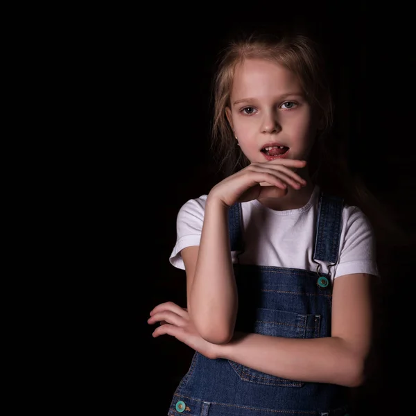 Hermosa niña rubia sobre un fondo oscuro. Ella se para en diferentes poses y muestra diferentes emociones. espacio libre para su texto — Foto de Stock