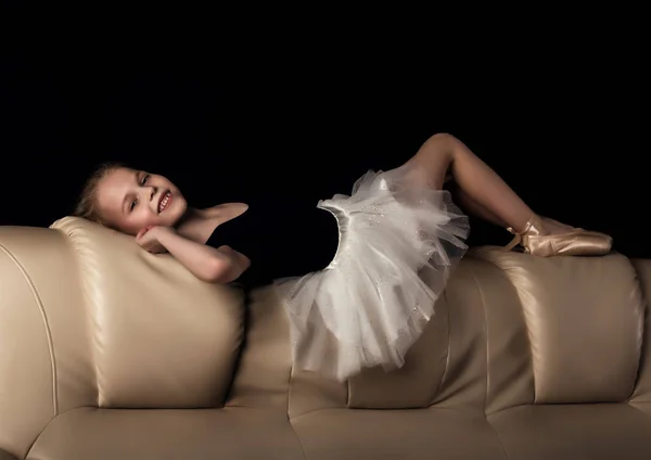 Маленькая балерина в пуанте сидит и отдыхает на диване. милая балерина в танцевальном классе изучает балет. Классический танец, балет — стоковое фото