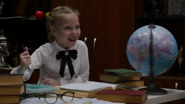 Школьница делает домашнее задание, маленькая блондинка заигрывает дома за столом. воспитание детей. 4K — стоковое видео