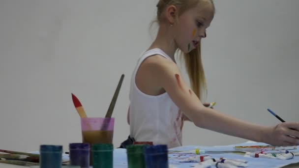 Söt liten flicka målare drar på bordet och på sig själv på hennes kläder. Slow motion — Stockvideo