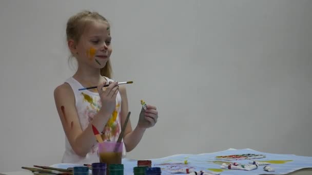 Schattige kleine meisje schilder trekt op de tafel en op zichzelf op haar kleren. Slow Motion — Stockvideo