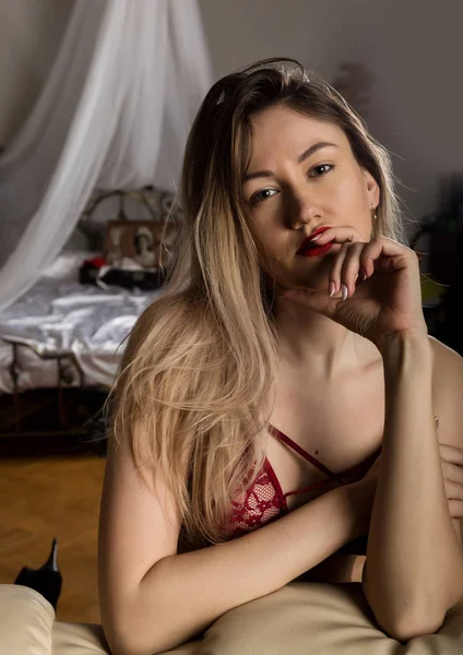 Lákavá mladá dáma v červené podprseně, která odpočívá na pohovce v hotelovém pokoji. sexy hipsterová dívka požívající na gauči — Stock fotografie