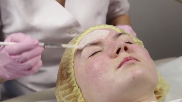 Cosmetologist que aplica a máscara facial à pele do problema. mulher jovem com procedimentos de limpeza da pele — Vídeo de Stock