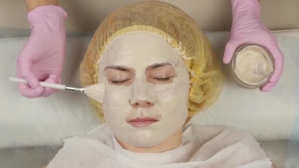 Косметолог надевает маску для лица на проблемную кожу. молодая женщина, проходящая чистку кожи. 4K — стоковое видео