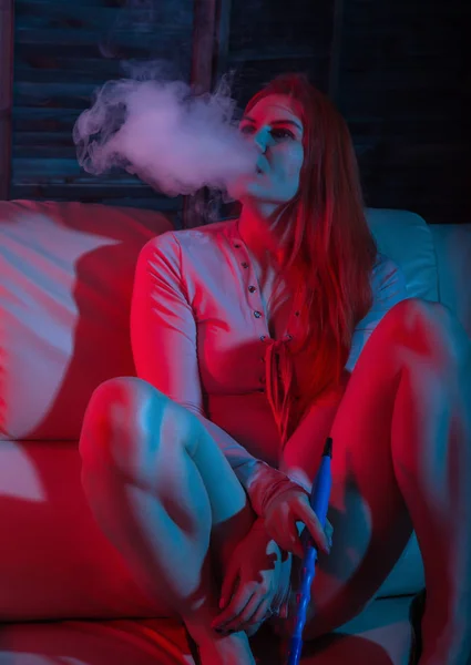 Sexy zrzavá žena s elektronickým hookahem v červených modrých tónech — Stock fotografie