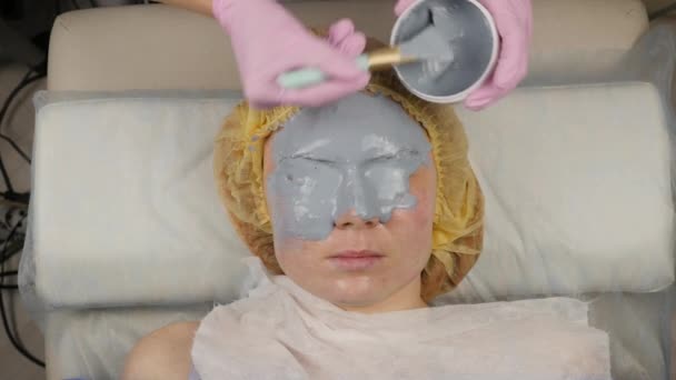Косметолог надевает маску для лица женщины в спа-салоне. процедуры омоложения лица, спа-процедуры — стоковое видео
