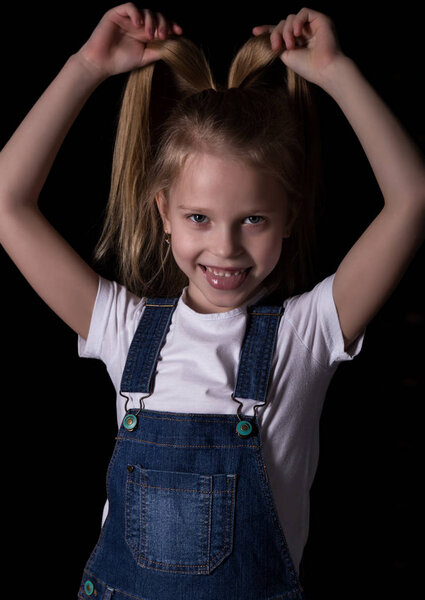 beautiful blonde little girl on a dark background. She stands in different poses and shows different emotions