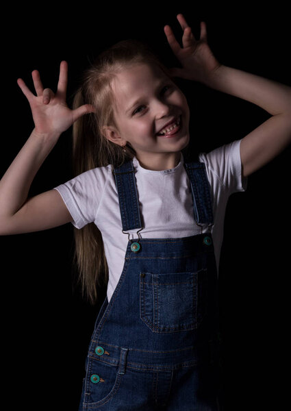 beautiful blonde little girl on a dark background. She stands in different poses and shows different emotions