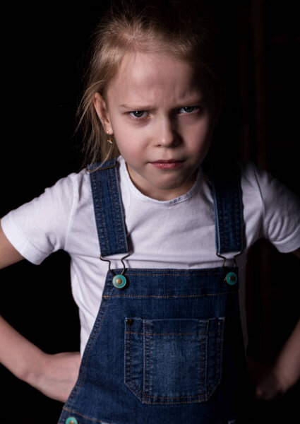 beautiful blonde little girl on a dark background. She stands in different poses and shows different emotions