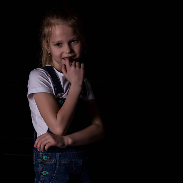 beautiful blonde little girl on a dark background. She stands in different poses and shows different emotions. free space for your text