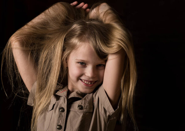 funny lovely little blonde child with different emotions on a dark background. beautiful schoolgirl holding herself hair