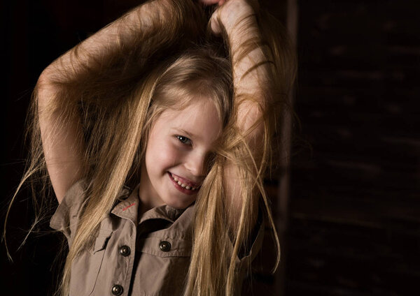 funny lovely little blonde child with different emotions on a dark background. beautiful schoolgirl holding herself hair
