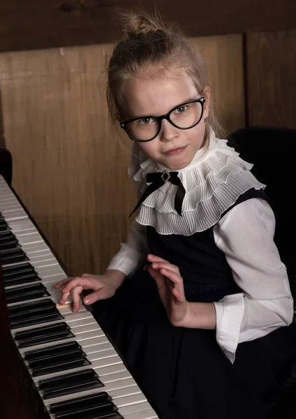 Сувора маленька дівчинка у великих окулярах грає на піаніно, дитина імітує вчителя — стокове фото