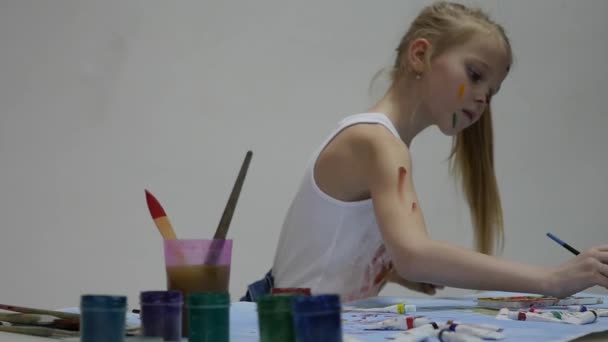 Pequeña colegiala. Lindo pintor niña dibuja en la mesa y en sí mismo en su ropa. cámara lenta — Vídeos de Stock