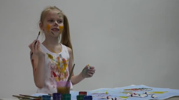 Klein school meisje. Schattige kleine meisje schilder trekt op de tafel en op zichzelf op haar kleren. Slow Motion — Stockvideo