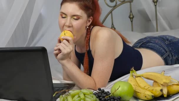 Mujer pelirroja come fruta fresca mientras está acostada en la cama. desayuno saludable. cámara lenta — Vídeo de stock