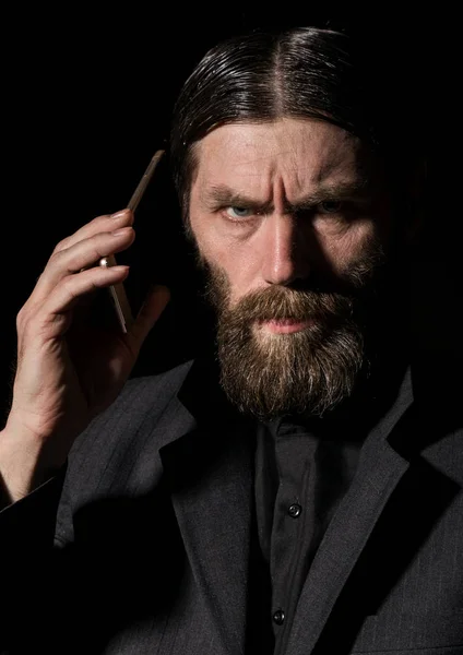 Bir akıllı telefon ile eski mümin Kıdemli Rahip, sakallı yaşlı adam karanlık bir arka planda çağırıyor — Stok fotoğraf