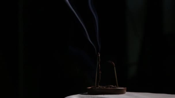 Paus de incenso queimando, fumaça azul flui lentamente em um fundo escuro — Vídeo de Stock