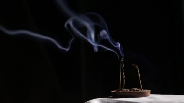 Τα ραβδιά θυμίαμα καίγονται, ο Γαλάζιος καπνός ρέει αργά σε σκούρο φόντο — Αρχείο Βίντεο