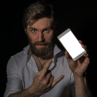 yakışıklı sakallı adam karanlık bir arka plan üzerinde büyüleyici bir gülümseme ile telefonunu gösterir.