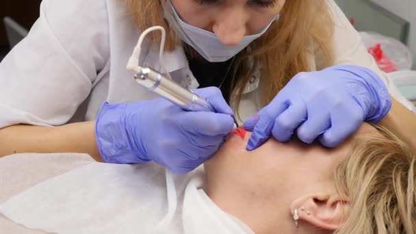 Врач-косметолог проводит процедуру перманентного макияжа женских губ клиента. замедленное движение — стоковое видео