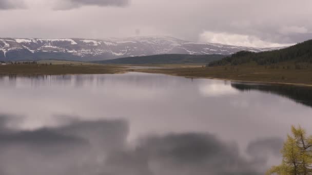 Вид на гірське озеро з штормовими хмарами, відображеними на водяній поверхні. сніг на вершинах гір — стокове відео