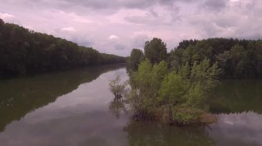 Havadan görünüm. Güneşli yaz sabahı göl üzerinde düşük uçuş. Yeşil ağaçlar ve tepeler, göl yüzeyindeki bulutların yansıması. 4k