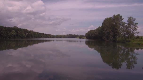 Вид с воздуха. Низкий полет над озером в солнечное летнее утро. Зеленые деревья и холмы, отражение облаков на поверхности озера. 4K — стоковое видео