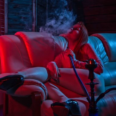 Seksi redhead hipster kadın elektronik nargile vaping. kız kırmızı mavi tonları büyük duman dışarı darbeler.