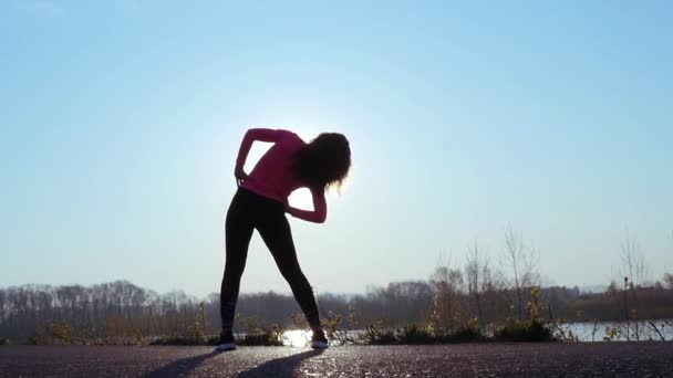 Die sportliche Frau treibt bei Sonnenaufgang Sport am Ufer des Flusses. Zeitlupe — Stockvideo