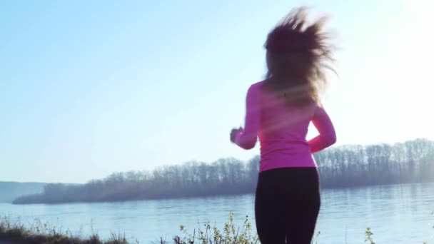 Sportliches Mädchen, das bei Sonnenaufgang oder Sonnenuntergang am Ufer des Flusses joggt. gesunder Lebensstil Konzept der athletischen Frau geht in den Sport. Zeitlupe — Stockvideo