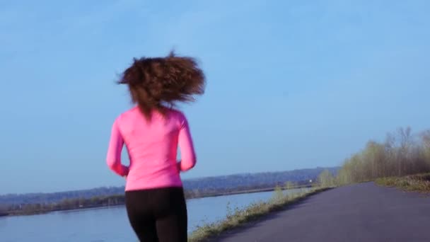 Спортивная девушка бегает вдоль берега реки на рассвете или на закате. Занимается спортом концепция здорового образа жизни спортивной женщины. замедленное движение — стоковое видео