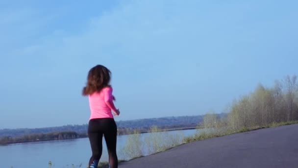 Sportiga flicka jogging längs floden banken under soluppgång eller solnedgång. hälsosam livsstil begreppet atletisk kvinna går in för sport. Slow motion — Stockvideo