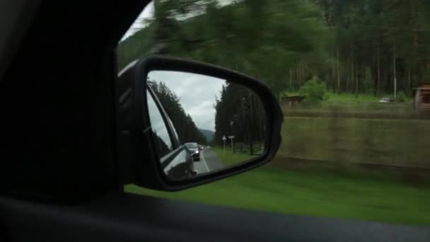 Vista del espejo lateral, reflejo de un camino de montaña a través del campo en un día de verano — Vídeos de Stock