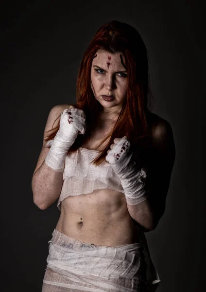 young redhead female fighter after the fight in a dark. girls in martial arts. bloody bandages with fists