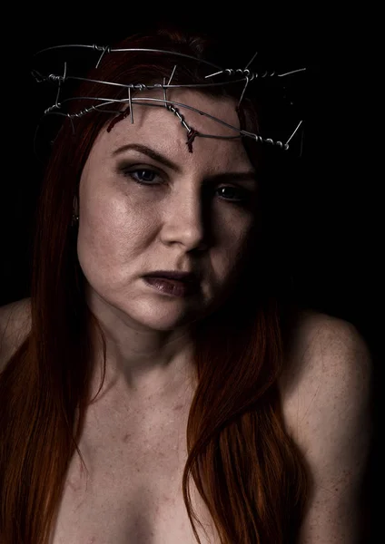 Tourmenté belle femme avec une couronne de fil de fer barbelé sur la tête sur un fond sombre — Photo