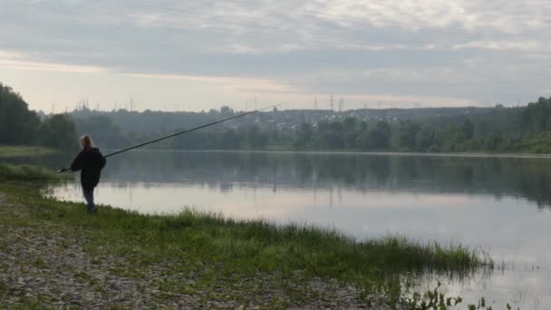 Mignon adolescent fille pêche sur la rive de la rivière debout sur le sable et tenant canne à pêche . — Video