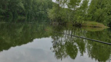 sakin bir su gölde ısırıkları bekliyor olta. su üzerinde hafta sonu. 4k. suyun yüzeyinde bulutlar ve ağaçların yansıması