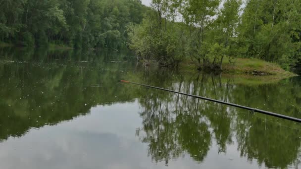 Vara de pesca à espera de mordidas em um lago de água calma. fim de semana na água. 4K. reflexão de nuvens e árvores na superfície da água — Vídeo de Stock
