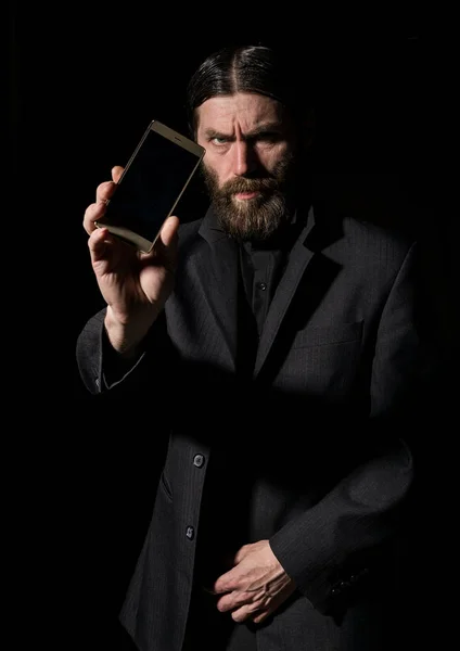 Странный бородатый первосвященник со смартфоном, бородатый старик зовет на темный фон — стоковое фото