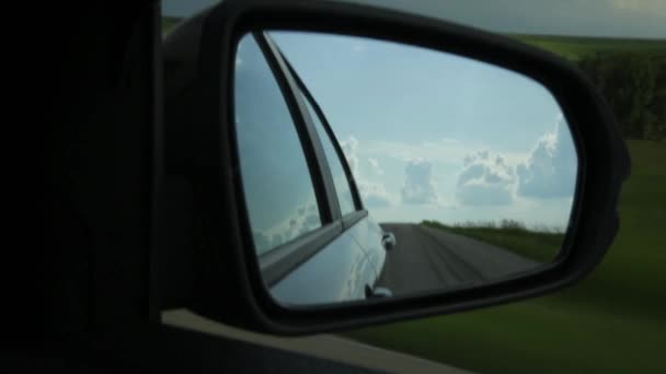 Вид збоку дзеркала в машині, відображення хмар і сільської дороги через сільську місцевість в літній день — стокове відео