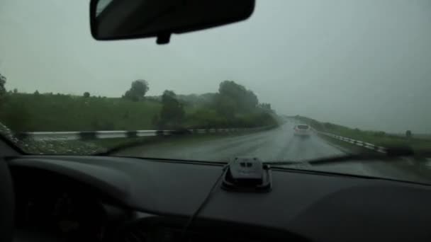 Вождение в неприятный дождливый день, приборная панель и руль с водителями руками, капли дождя на окно автомобиля лобовое стекло — стоковое видео