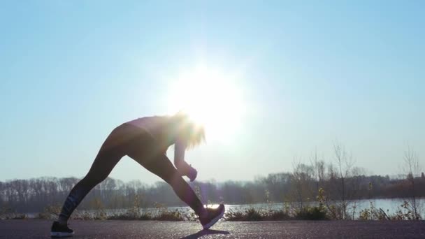 Die sportliche Frau treibt bei Sonnenaufgang Sport am Ufer des Flusses. Zeitlupe — Stockvideo