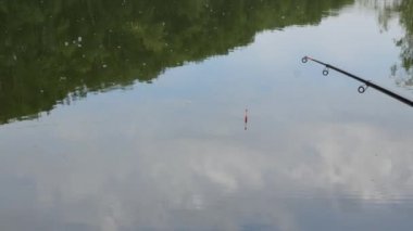 sakin bir su gölde ısırıkları bekliyor olta. su üzerinde hafta sonu. suyun yüzeyinde bulutlar ve ağaçların yansıması.