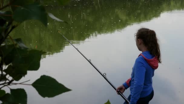 Mignon adolescent fille pêche sur la rive de la rivière debout sur le sable et tenant canne à pêche . — Video