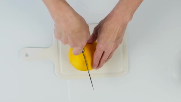 Confiseur à l'aide d'un couteau coupé une oranges. deux moitiés d'orange sur une planche à découper. 4K vue de dessus — Video